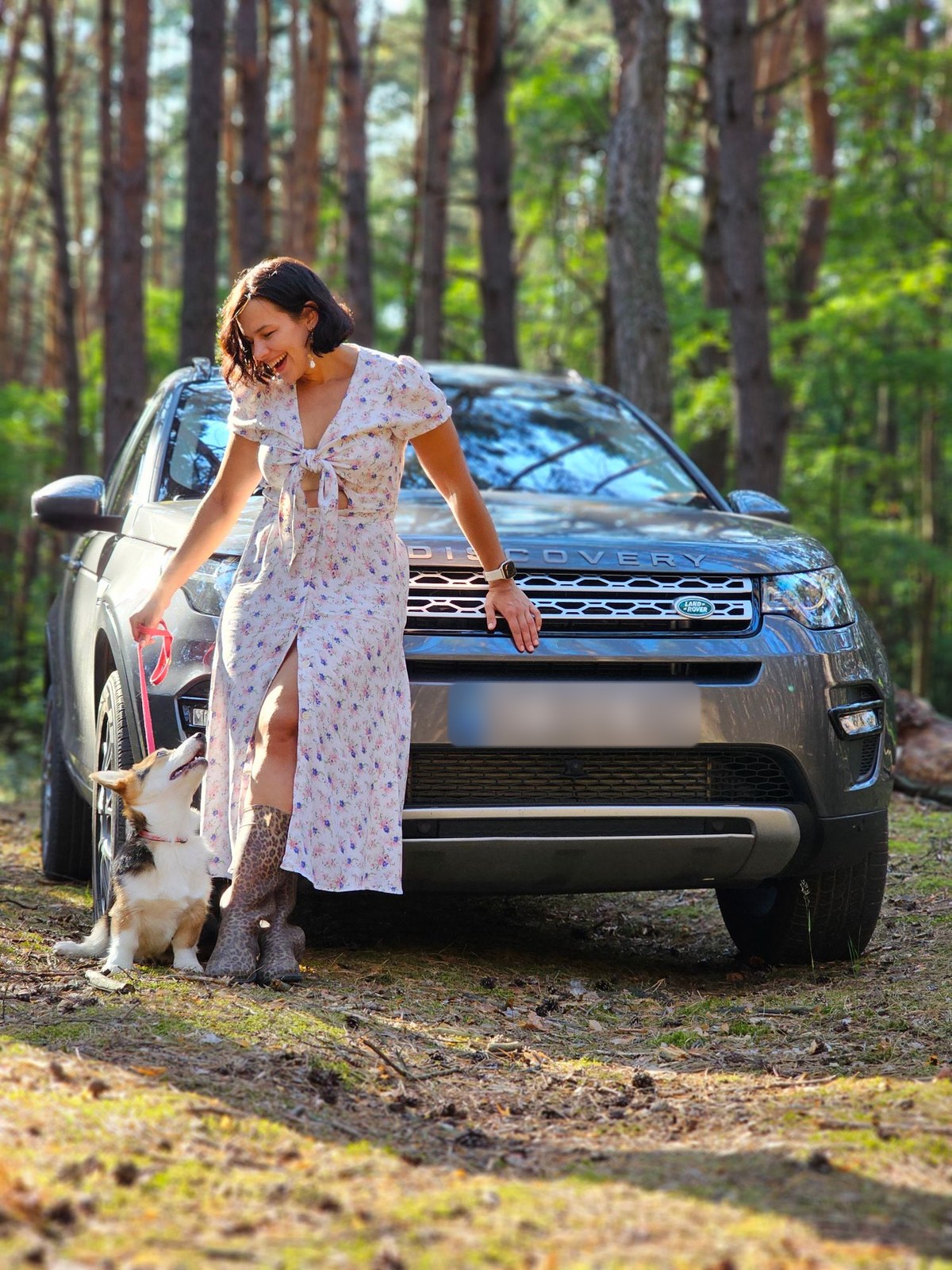 Учасниця клубу з коргі біля сірого Land Rover Discovery Sport у сосновому лісі