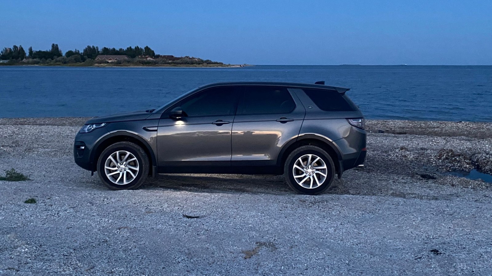 Сірий Land Rover Discovery Sport учасника клубу на березі моря в сутінках
