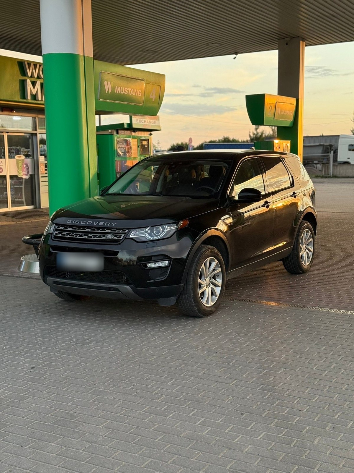 Чорний Land Rover Discovery Sport учасника клубу на заправці на заході сонця